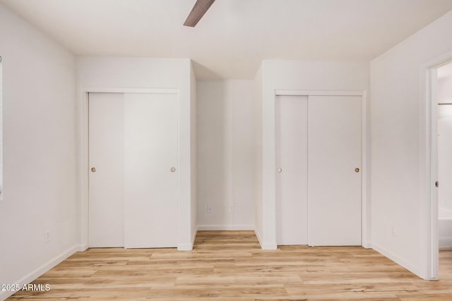 unfurnished bedroom featuring light wood-type flooring, baseboards, and two closets