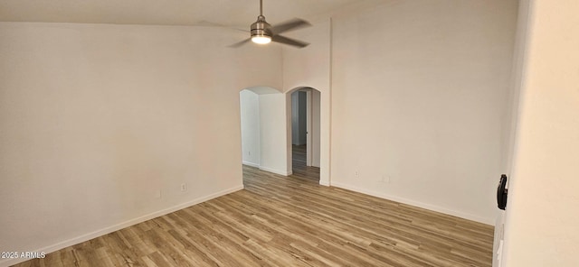 empty room featuring baseboards, a ceiling fan, light wood finished floors, and arched walkways