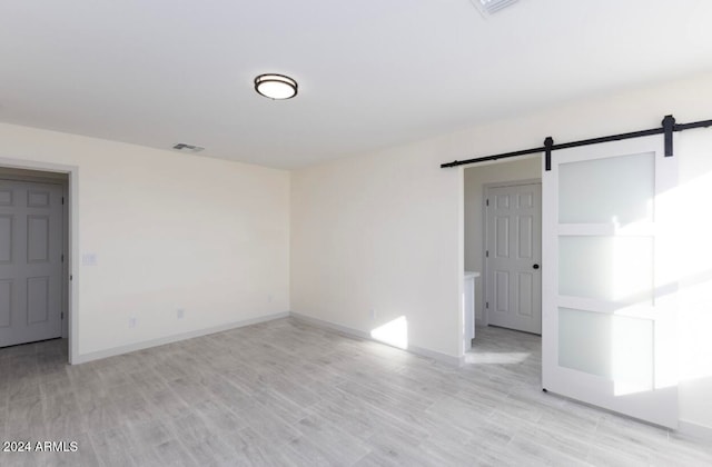 unfurnished room with a barn door and light hardwood / wood-style floors