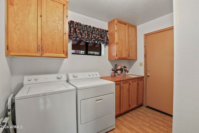 laundry area with cabinets, light hardwood / wood-style floors, washing machine and dryer, and a textured ceiling