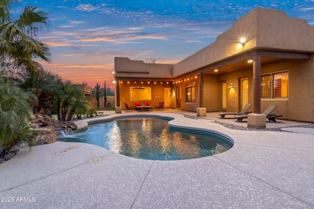 pool at dusk with a patio and pool water feature