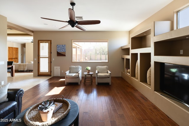 living room with built in shelves, ceiling fan, and dark wood-type flooring