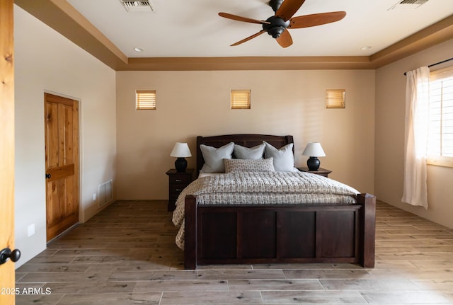 bedroom featuring ceiling fan, light hardwood / wood-style floors, and a raised ceiling