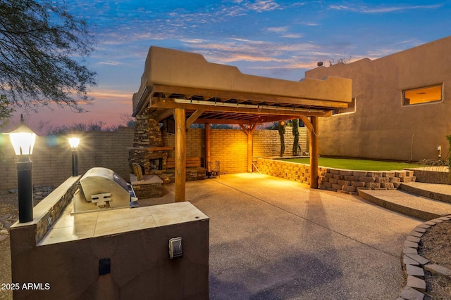 patio terrace at dusk with area for grilling and an outdoor stone fireplace