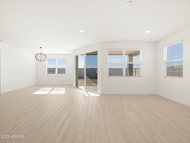 spare room featuring an inviting chandelier, light wood-type flooring, and plenty of natural light