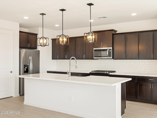 kitchen with appliances with stainless steel finishes, pendant lighting, dark brown cabinets, and a center island with sink