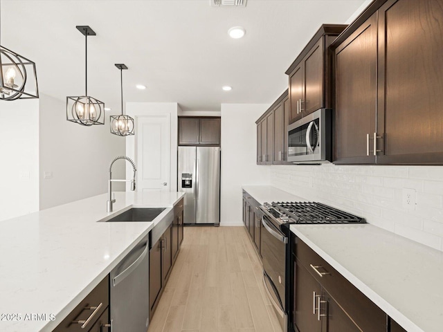 kitchen with light stone countertops, pendant lighting, dark brown cabinetry, appliances with stainless steel finishes, and sink