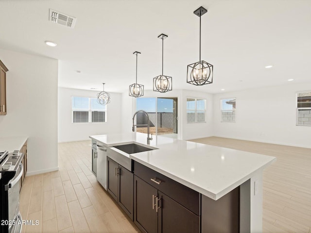 kitchen featuring sink, stainless steel appliances, dark brown cabinetry, a center island with sink, and pendant lighting