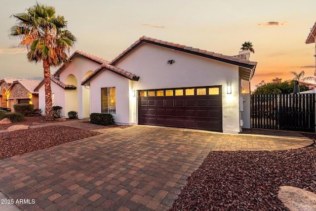 mediterranean / spanish-style home with a garage, decorative driveway, a chimney, and stucco siding