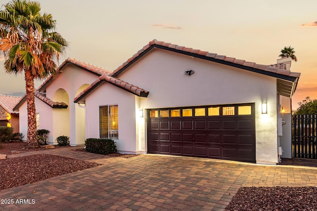 mediterranean / spanish home featuring decorative driveway, a chimney, an attached garage, and stucco siding