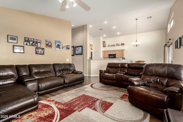 living room with hardwood / wood-style flooring, ceiling fan with notable chandelier, and high vaulted ceiling