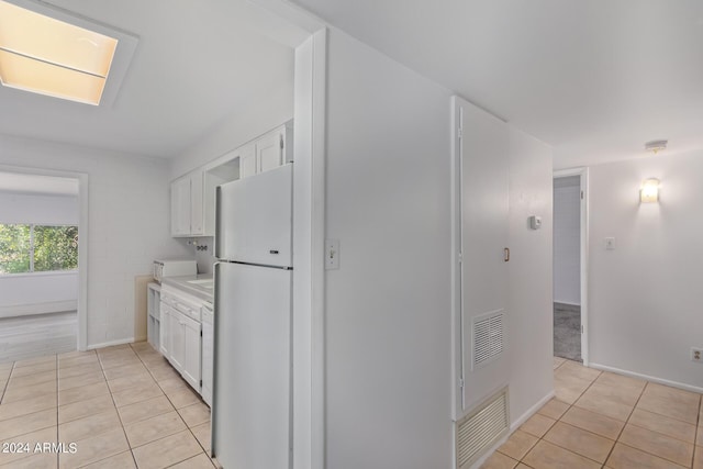 kitchen with light tile patterned flooring, white cabinets, light countertops, and freestanding refrigerator