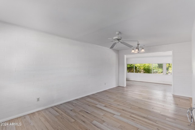 unfurnished room with ceiling fan with notable chandelier, brick wall, and wood finished floors