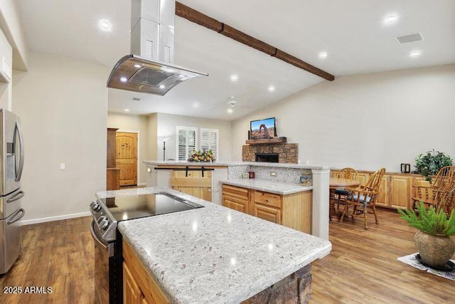 kitchen with lofted ceiling with beams, appliances with stainless steel finishes, wood finished floors, a large island with sink, and a fireplace