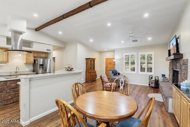 dining room with lofted ceiling with beams, ceiling fan, wood finished floors, a stone fireplace, and recessed lighting