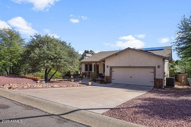 ranch-style home featuring driveway, a garage, fence, roof mounted solar panels, and stucco siding