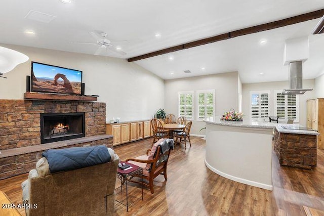 living area with vaulted ceiling with beams, ceiling fan, a fireplace, and wood finished floors