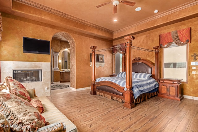 bedroom featuring ceiling fan, crown molding, connected bathroom, light hardwood / wood-style floors, and a tile fireplace