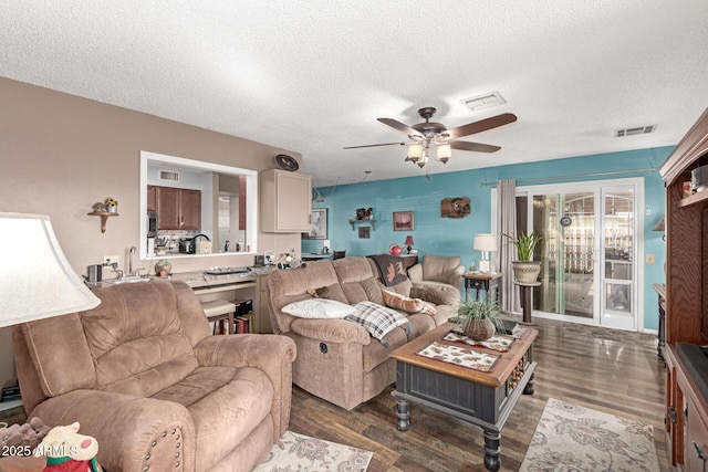 living room featuring visible vents, a textured ceiling, dark wood finished floors, and a ceiling fan