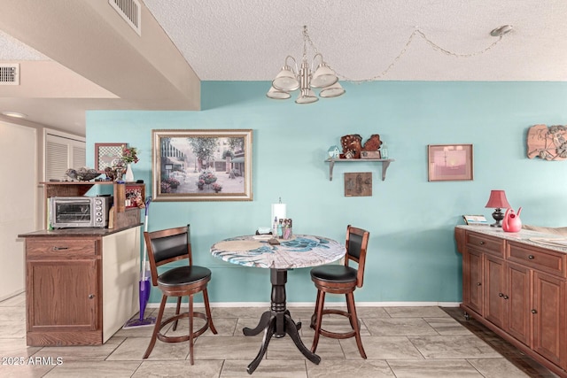 dining space featuring a toaster, visible vents, a textured ceiling, and an inviting chandelier