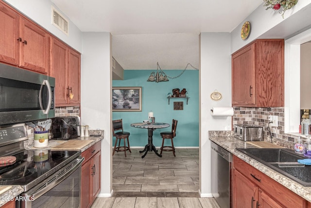 kitchen featuring tasteful backsplash, visible vents, wood finish floors, appliances with stainless steel finishes, and brown cabinetry