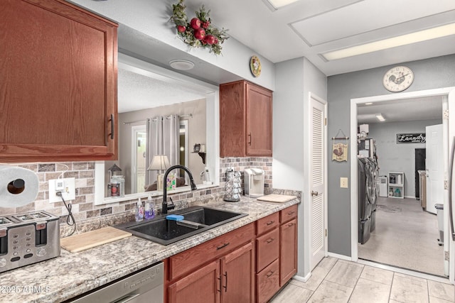 kitchen with a sink, backsplash, light countertops, independent washer and dryer, and stainless steel dishwasher