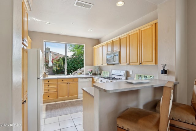 kitchen featuring visible vents, a peninsula, white appliances, and light brown cabinetry