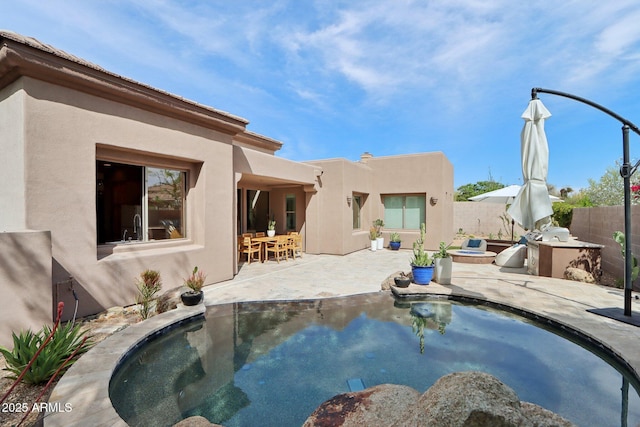 back of property featuring a patio area, fence, a fenced in pool, exterior kitchen, and stucco siding