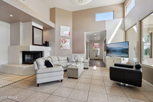 living area with a fireplace with raised hearth, a towering ceiling, baseboards, and light tile patterned floors