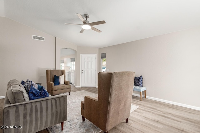 living area featuring arched walkways, visible vents, light wood-style floors, vaulted ceiling, and baseboards