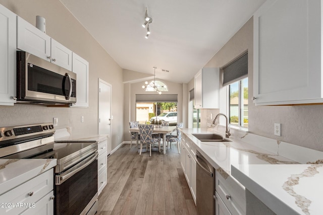 kitchen with appliances with stainless steel finishes, vaulted ceiling, light wood-style floors, white cabinetry, and a sink