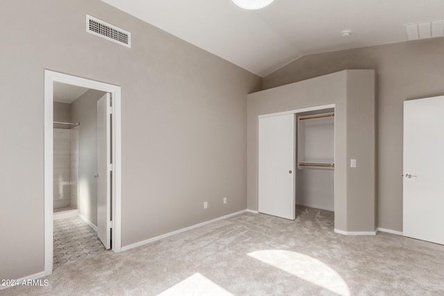 unfurnished bedroom featuring lofted ceiling, ensuite bathroom, light carpet, visible vents, and a closet