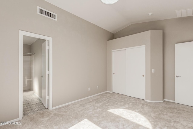 unfurnished bedroom with lofted ceiling, a closet, visible vents, and light carpet