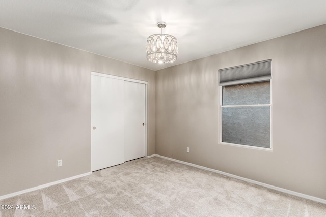 empty room with light carpet, an inviting chandelier, and baseboards