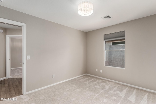 empty room featuring a chandelier, light carpet, visible vents, and baseboards