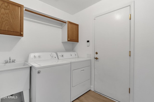 clothes washing area with independent washer and dryer, sink, cabinets, and light wood-type flooring