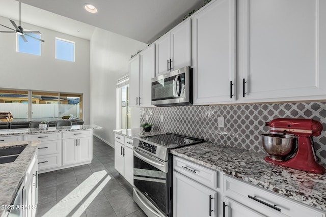 kitchen with dark tile patterned flooring, backsplash, white cabinetry, and stainless steel appliances