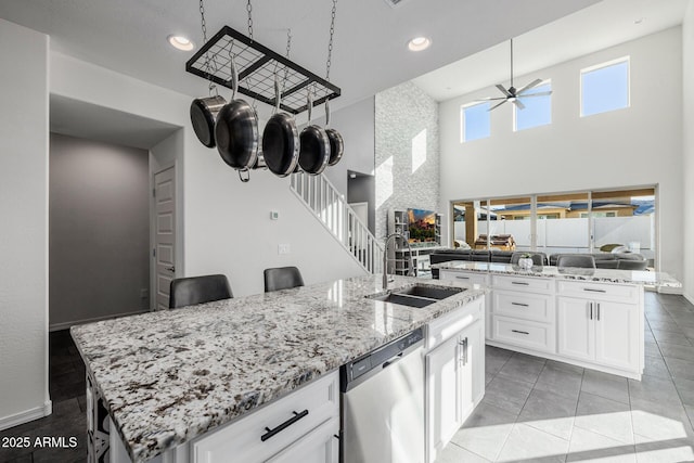 kitchen featuring stainless steel dishwasher, sink, white cabinets, a high ceiling, and an island with sink