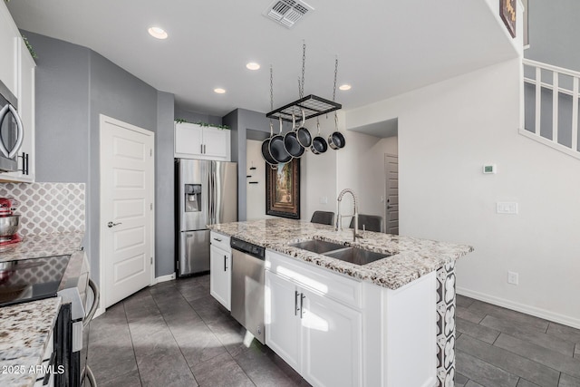 kitchen featuring appliances with stainless steel finishes, sink, white cabinets, light stone counters, and a center island with sink