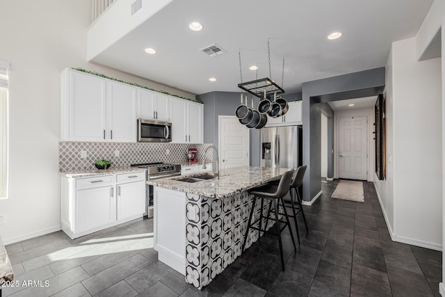 kitchen with appliances with stainless steel finishes, sink, white cabinetry, light stone countertops, and a center island with sink