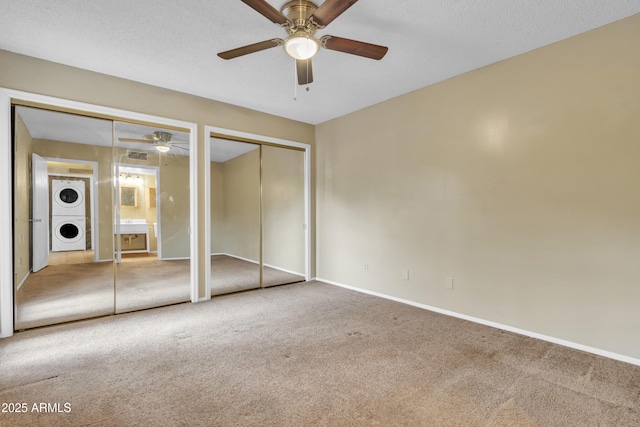 unfurnished bedroom with two closets, carpet floors, stacked washer and dryer, and baseboards