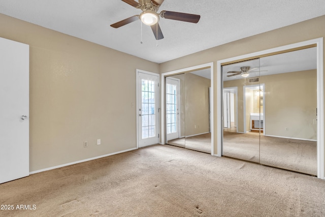 unfurnished bedroom featuring visible vents, baseboards, carpet, ceiling fan, and two closets