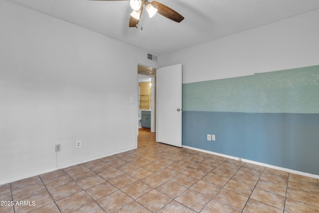 empty room featuring tile patterned flooring, visible vents, baseboards, a textured ceiling, and ceiling fan