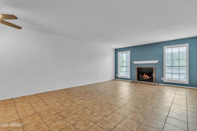 unfurnished living room with a textured ceiling, baseboards, a ceiling fan, a brick fireplace, and light tile patterned floors
