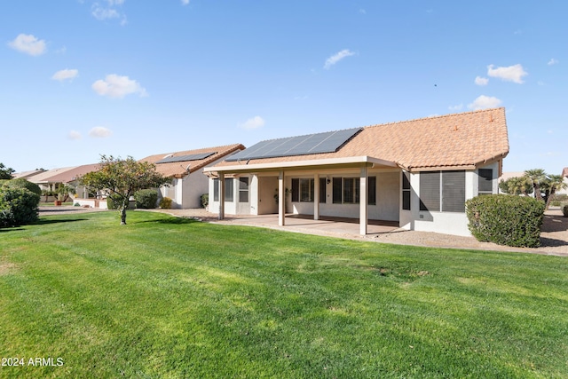 back of property with solar panels, a patio area, and a yard