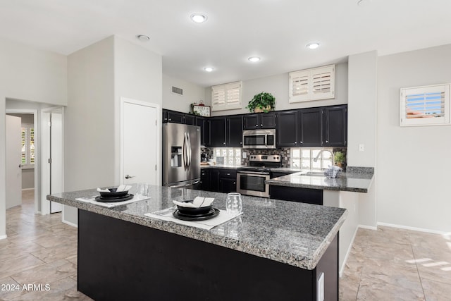 kitchen with sink, stainless steel appliances, light stone counters, kitchen peninsula, and decorative backsplash