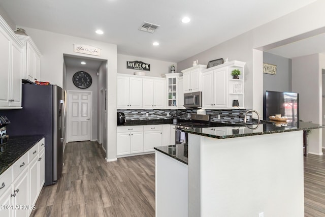 kitchen featuring white cabinetry, kitchen peninsula, wood-type flooring, decorative backsplash, and appliances with stainless steel finishes