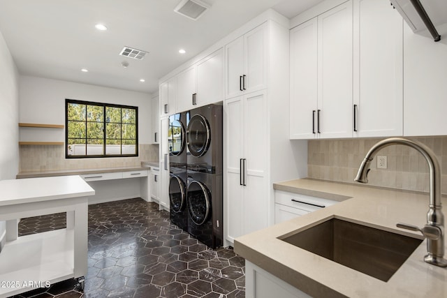 kitchen with stacked washer / drying machine, decorative backsplash, sink, and white cabinets