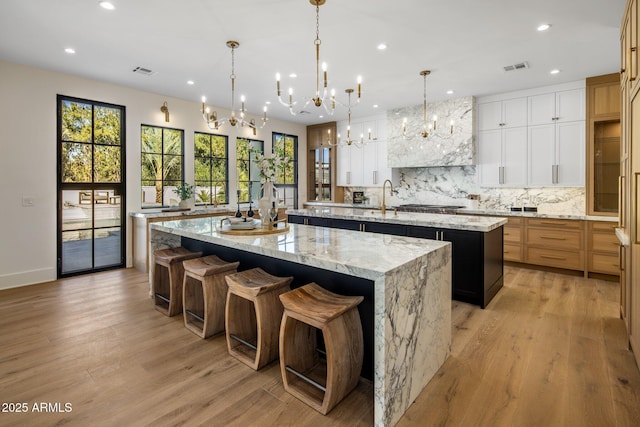 kitchen with visible vents, a large island with sink, light wood finished floors, and decorative backsplash