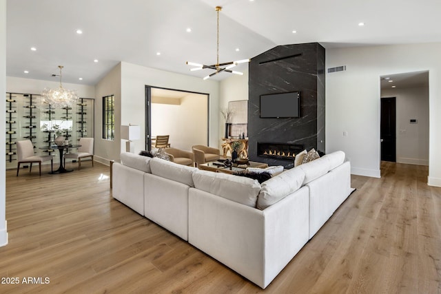 living room featuring a fireplace, vaulted ceiling, a chandelier, and light wood-type flooring